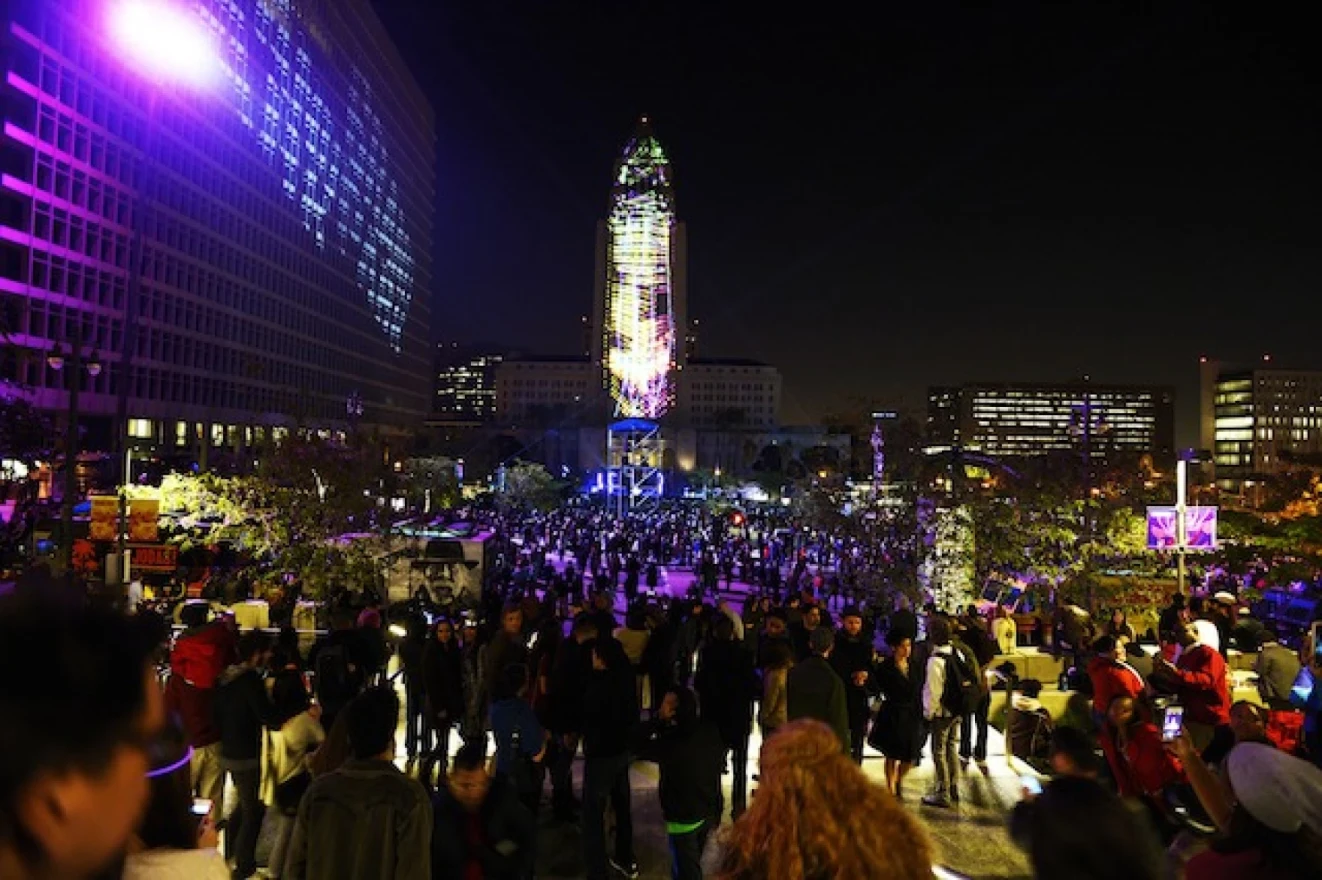 New Year's Eve revelers gather in the plaza of Grand Park in Los Angeles as a variety of lights paint the space in pink, purple, and blue.